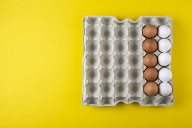 Renkli sarı arka planlı, karton yumurta kutusunda güzel, büyük, kırsal, taze yumurtalar. Metin için boşluk.