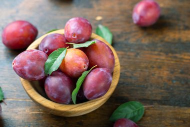 Masadaki ahşap bir kasede olgun erikler ve yapraklar. Hasat mevsimi.