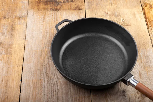 Empty cast iron pan on wooden culinary background, space for text. Top view.