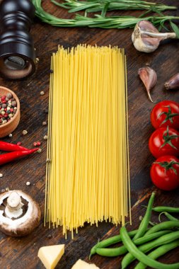 Taze domatesli çiğ makarna, biber, kuşkonmaz fasulyesi, baharat ve peynir ahşap bir masada. İtalyan spagettisi için yemek malzemeleri..