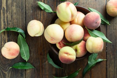 Ahşap bir kırsal masada, kil bir kasede taze şeftali hasadı. Şeftali yaprakları kompozisyonda mevcuttur. Organik meyve, vejetaryen yemeği..