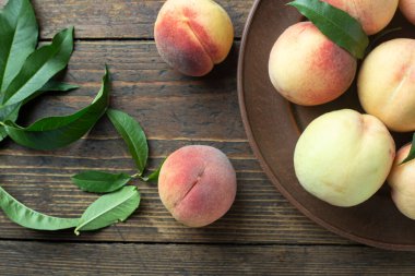 Tahta bir masada, kil bir tabakta yapraklarla olgunlaşmış şeftaliler. Taze hasat. Üst görünüm.