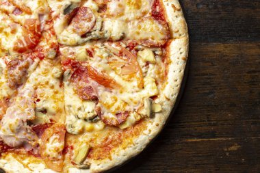 Tahta arka planda pastırmalı, domatesli, mantarlı ve peynirli taze İtalyan pizzası. İtalyan yemeği. Mesaj için yer var. Üst görünüm.