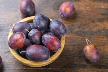Kahverengi bir masada, tahta bir kasede taze erikler. Yaz hasadı toplanıyor..