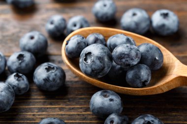 Tahta kaşıkta taze yaban mersini. Böğürtlenler ahşap bir masaya saçılmış. Vejetaryen ve vejetaryen kavramı. Antioksidan özelliği olan ürünler.