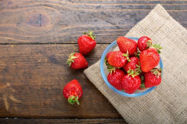Ahşap bir masada cam bir kasede çilekler..