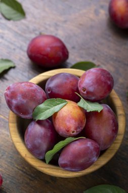 Kahverengi bir masada, ahşap bir kasede yaprakları olan taze erikler. Yaz hasadı toplanıyor..