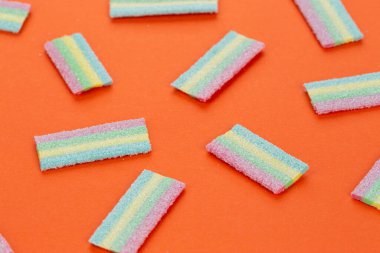 Turuncu arka planda renkli şekerleme deseni. Yumuşak diş etleri yukarıdan görünüyor. Çeşitlilik konsepti. Eşcinsel renkleri. Tatlı yemek tatlısı. Yukarıdan görüntüle