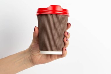 Beyaz arka planda tek kullanımlık kahve fincanının kahverengi rengini tutan kadın eli. Yakın plan..