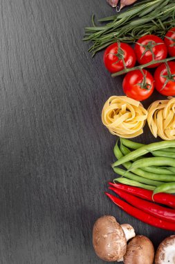 Çiğ makarna tagliatelle taze domates, biber, kuşkonmaz fasulyesi, baharat ve peynirli siyah masa. İtalyan spagettisi için yemek malzemeleri. Mesaj için yer var. Üst görünüm.