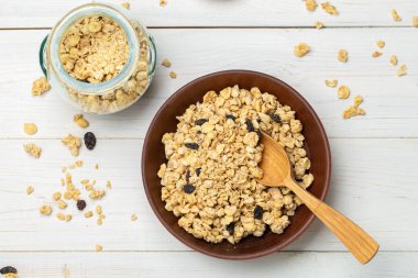 Sağlıklı kahvaltı. Beyaz ahşap bir masada, kuru üzümlü bir kase içinde müsli. Müsli masanın üzerine dağıldı. Mesaj için yer var. Üst görünüm.