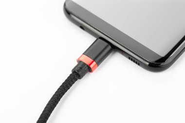 Beyaz arka planda şarj kablosu olan bir cep telefonu. Hücresel iletişim kavramı.
