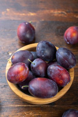 Kahverengi bir masada, tahta bir kasede taze erikler. Yaz hasadı toplanıyor..