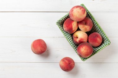 Beyaz ahşap arka planda sepetin içinde taze, olgun şeftaliler. Lezzetli ve sağlıklı meyveler. Sağlıklı gıda konsepti.
