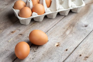 Karton bir kutuda kahverengi yumurtalar. Yumurtalar ahşap zemine saçılmış. Sağlıklı gıda konsepti. Çiftlik işçiliği ve bakımı.