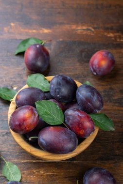 Kahverengi bir masada, ahşap bir kasede yaprakları olan taze erikler. Yaz hasadı toplanıyor..