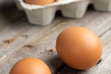 Karton bir kutuda kahverengi yumurtalar. Yumurtalar ahşap zemine saçılmış. Sağlıklı gıda konsepti. Çiftlik işçiliği ve bakımı.