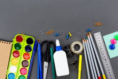 Okul malzemeleri gri bir zemine saçılmış. Mesaj için yer var. Üst görünüm