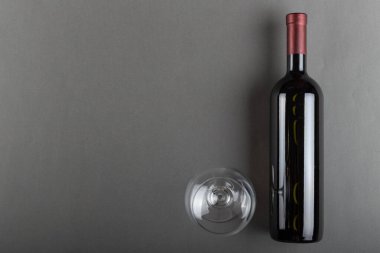 Mantarlı kırmızı şarap şişesi ve gri arka planda boş şarap kadehi. Alkolik içki. Şarap yapma konsepti. Mesaj için yer var. Üst görünüm.