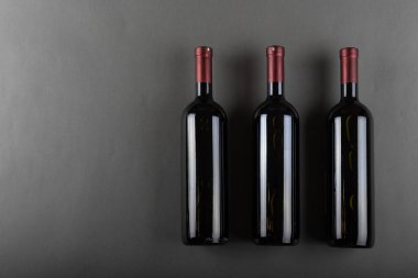 Gri bir ofiste tıpalanmış üç şişe kırmızı şarap. Alkolik içki. Şarap yapma konsepti. Mesaj için yer var. Üst görünüm.