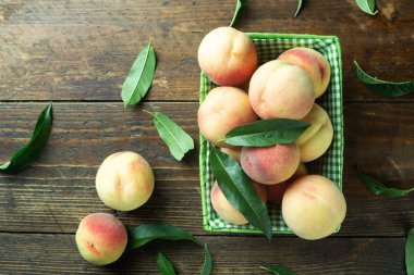 Tahta bir masada, yaprakları dökülmüş sepetin içinde olgun şeftaliler. Taze ev yapımı meyveler. Üst görünüm.