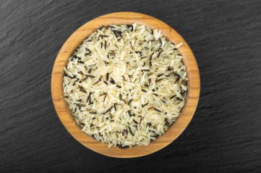 Wild rice in a bowl against a black background. Traditional food of oriental cultures.