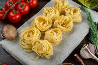 Çiğ makarna tagliatelle taze domates, biber, kuşkonmaz fasulyesi, baharat ve ahşap zemin üzerinde peynir. İtalyan spagettisi için yemek malzemeleri..