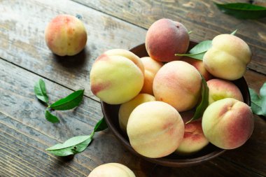 Ahşap bir kırsal masada, kil bir kasede taze şeftali hasadı. Şeftali yaprakları kompozisyonda mevcuttur. Organik meyve, vejetaryen yemeği..