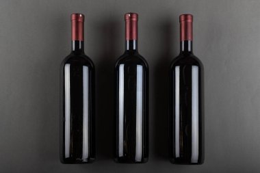 Gri bir ofiste tıpalanmış üç şişe kırmızı şarap. Alkolik içki. Şarap yapma konsepti. Mesaj için yer var. Üst görünüm.