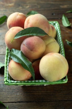 Tahta bir masada, yaprakları dökülmüş sepetin içinde olgun şeftaliler. Taze ev yapımı meyveler.