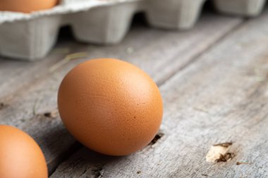 Karton bir kutuda kahverengi yumurtalar. Yumurtalar ahşap zemine saçılmış. Sağlıklı gıda konsepti. Çiftlik işçiliği ve bakımı.