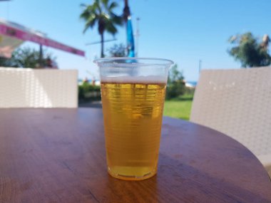 Plastik bardakta bira. Arka planda palmiye ağaçları ve deniz bulanık. Her şeyi kapsayan tatil konsepti.
