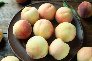 Tahta bir masada, yaprakları dökülmüş kil bir tabakta olgun şeftaliler. Taze ev yapımı meyveler.