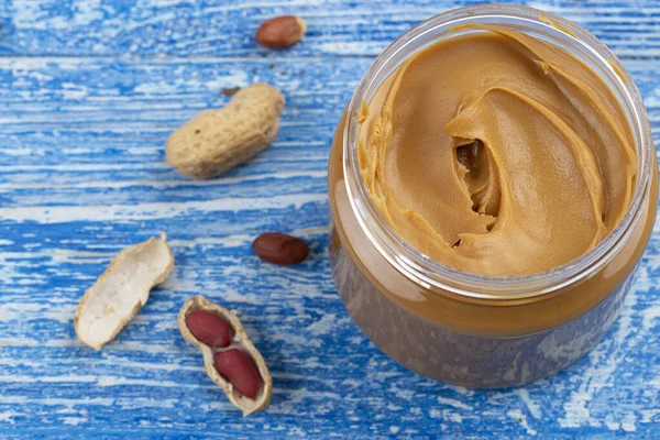 Açık kavanozdaki fıstık ezmesi ve derisindeki fıstıklar mavi masaya saçılmış. Mesaj için yer var. Yakın çekim..