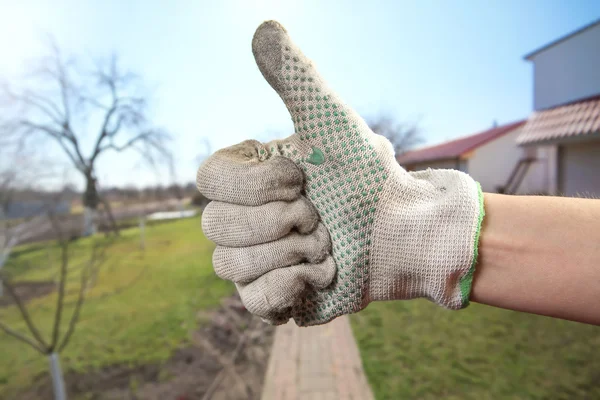 Schmutzige Handschuhe zur Hand. Handgeste zeigt, dass alles in Ordnung ist. Im Hintergrund ist ein Gartengrundstück — Stockfoto