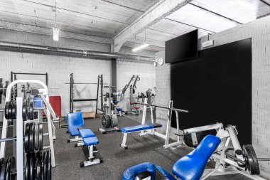 Klasik parlak bir spor salonu. Beyaz spor malzemeleri, mavi koltuklar ve siyah tahta. Ağırlığı farklı olan halterler