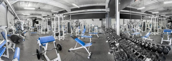 Panorama of a classic bright gym. White sport equipment and blue seats. Barbells of different weight on rack