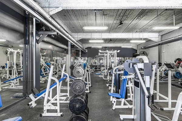 Panorama of a classic bright gym. White sport equipment and blue seats. Barbells of different weight on rack