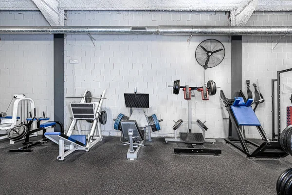 A classic bright gym. White sport equipment and blue seats. Barbells of different weight on rack