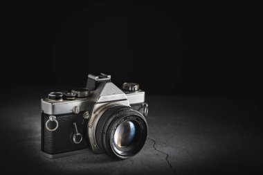 Taş zeminde sığ bir alan derinliği olan eski bir film retro kamerasının karanlık ürün fotoğrafçılığı. Fotokopi alanına sahip klasik görünümlü kamera teknolojisi kavramı.
