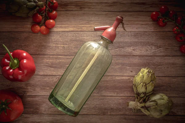 Flat lay retro food photography of an antique soda siphon, fresh cherry tomatoes, antique cutlery, artichokes and red pepper on a wood table. Still life image with a vintage look