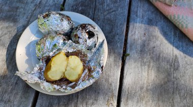 Sıcak kömürde ateşte pişmiş patates. Yemek, piknikte kamp ateşinin yanında folyoda sebzeler. Açık hava yemeği, akşam yemeği..