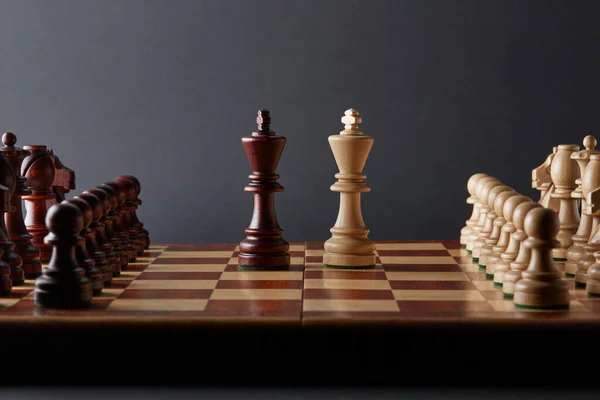 经典的木制锦标赛棋盘设置在黑色背景 两个国王站在棋盘中央 其他棋子排成一排 — 图库照片
