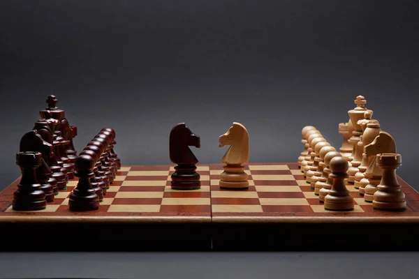 Classic Wooden Tournament chess set on black background. Two knights centre of board other pieces lined up