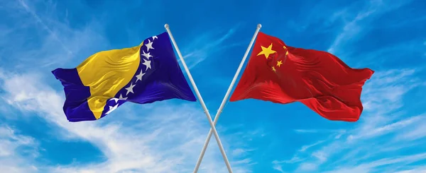 flags of China and Bosnia and Herzegovina waving in the wind on flagpoles against sky with clouds on sunny day. Symbolizing relationship, dialog between two countries. 3d illustration