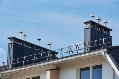 Metal levhalarla kaplı tuğla borunun ve çatıda siyah bir duman kutusunun yakın çekim görüntüsü. Modern evin çatısında havalandırma borusu var.