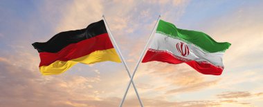 flags of Germany and Iran waving in the wind on flagpoles against sky with clouds on sunny day. Symbolizing relationship, dialog between two countries. 3d illustration,