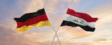 flags of Germany and Iraq waving in the wind on flagpoles against sky with clouds on sunny day. Symbolizing relationship, dialog between two countries. 3d illustration,