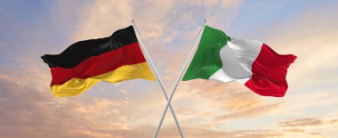 flags of Germany and Italia waving in the wind on flagpoles against sky with clouds on sunny day. Symbolizing relationship, dialog between two countries. 3d illustration,