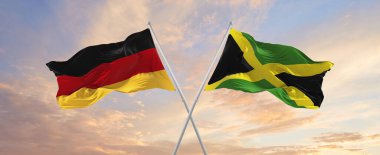 flags of Germany and Jamaica  waving in the wind on flagpoles against sky with clouds on sunny day. Symbolizing relationship, dialog between two countries. 3d illustration,